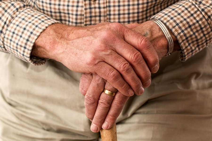 older person's hands holding a walking stick