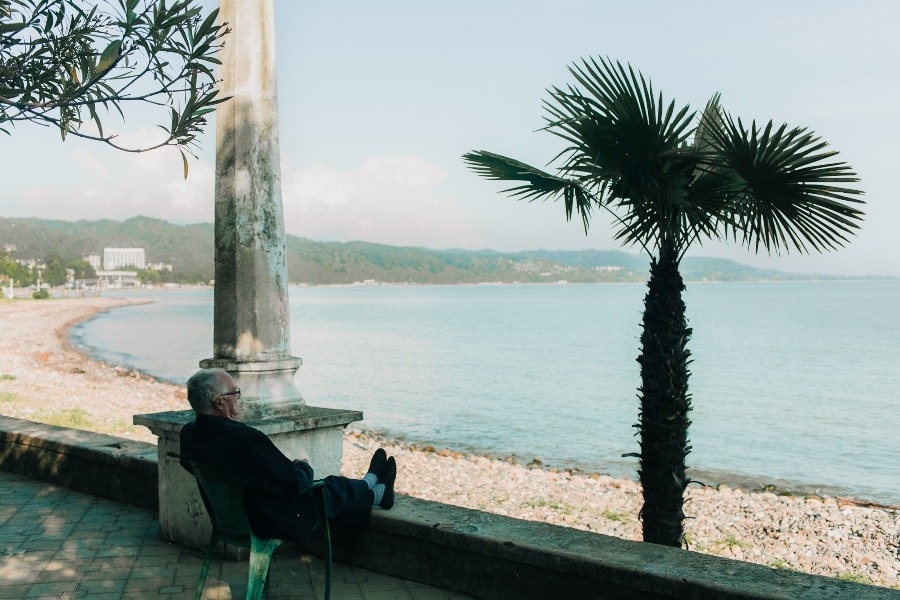 man sitting on plastic chair overlooking sunny beach